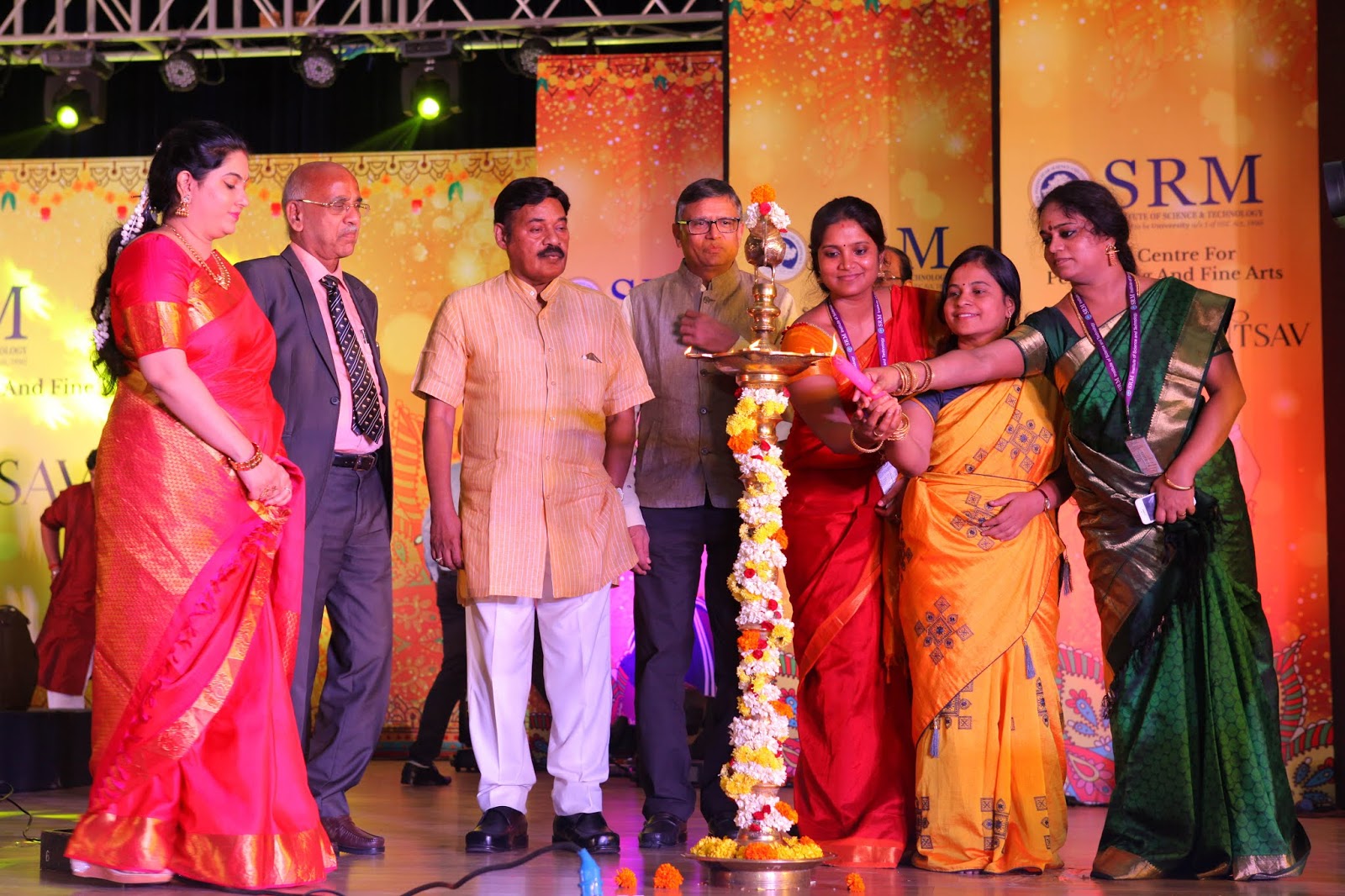 Dr. T. R. Paarivendhar with guests in traditional dress on a stage, as a woman lights a flower-garlanded brass lamp in front of an SRM Centre for Music and Fine Arts backdrop