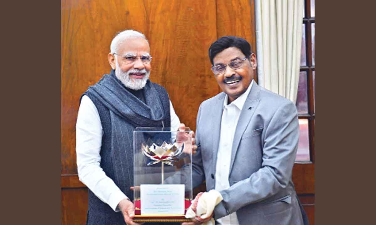 Dr. T. R. Paarivendhar in a grey suit standing beside Prime Minister Narendra Modi, the two holding a glass case containing a lotus memento