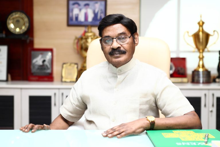Dr. T. R. Paarivendhar seated at his desk in an office lined with trophies, plaques and framed photographs